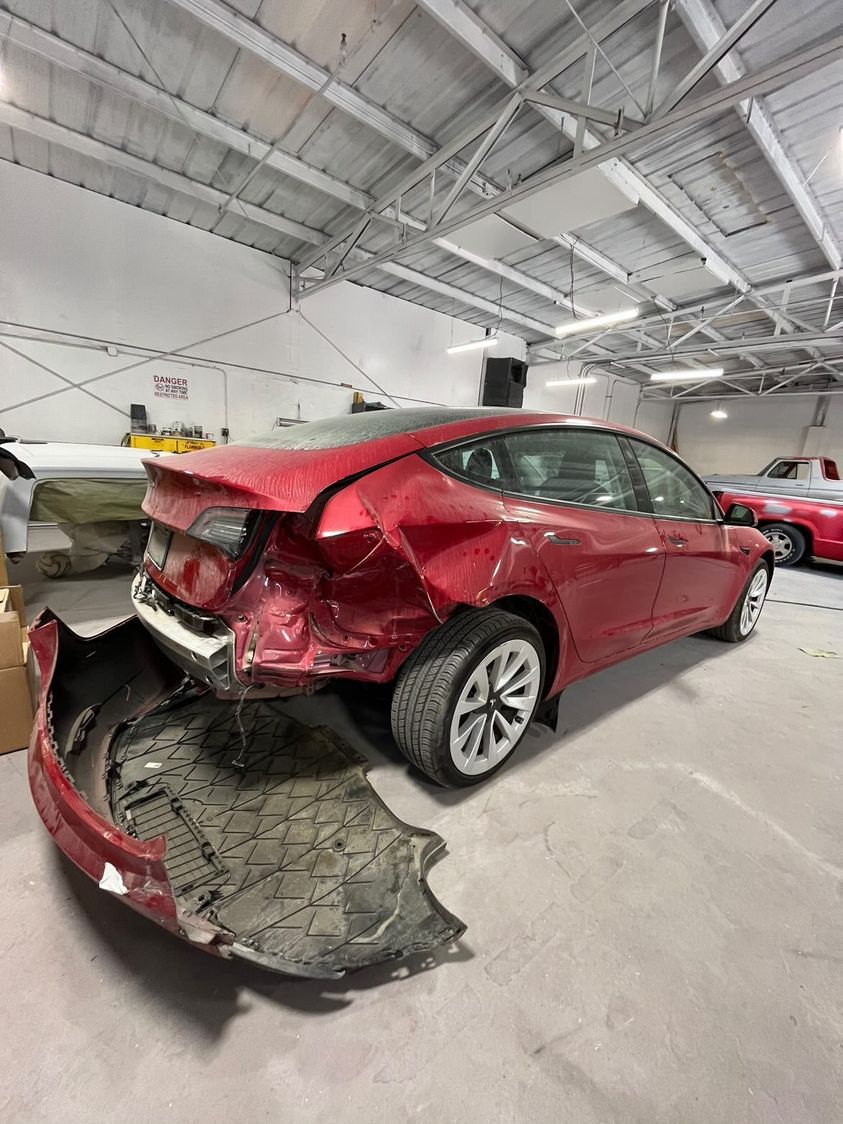 Red sedan with heavy rear-end collision damage in the shop